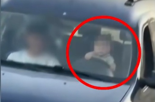 Un copil foarte mic la volanul unei mașini în mișcare, pe drum public. Mama de 17 ani îl filma
